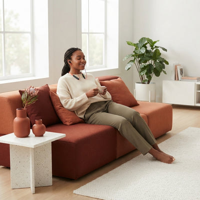 A person wearing a black Bluetooth wireless neckband while relaxing in a bright, modern living room with terracotta decor.