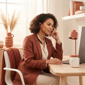 A person wearing a sleek wireless neckband in a bright, modern office with soft terracotta-toned decor.